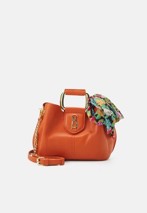 Sac à main en cuir orange avec poignée carrée dorée, tissu floral noué sur le côté, bandoulière chaîne dorée et logo doré à l'avant.