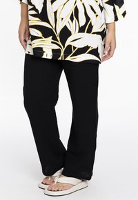 Zwarte textuur pants met een relaxte pasvorm, met een gekreukt stofafwerking. Gecombineerd met lichtgekleurde, platte sandalen.