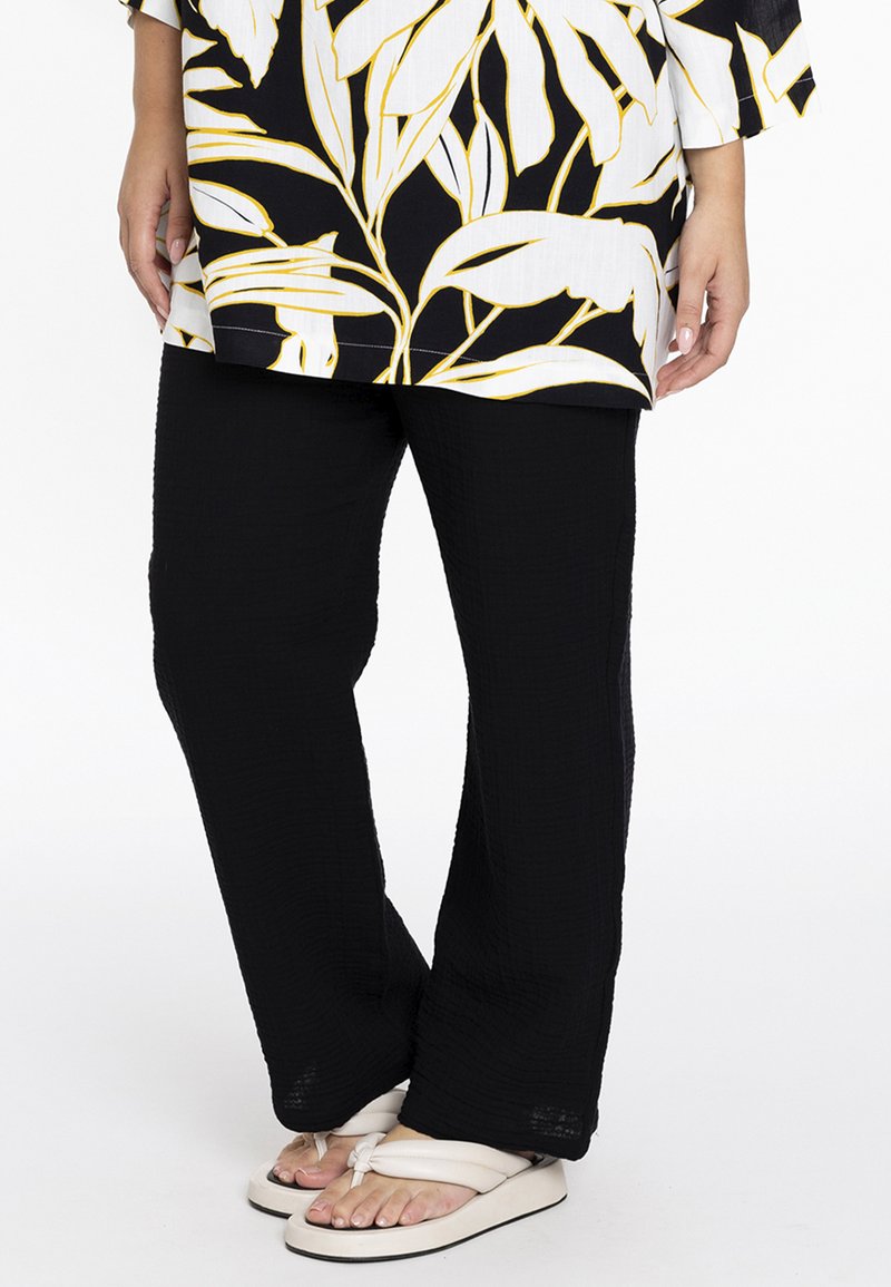Zwarte textuur pants met een relaxte pasvorm, met een gekreukt stofafwerking. Gecombineerd met lichtgekleurde, platte sandalen.