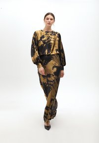 Lange goud- en zwart tie-dye jurk met een relaxed fit, lage vlindermouwen en een slanke silhouet. Gepaard met scherpe zwarte hakken.