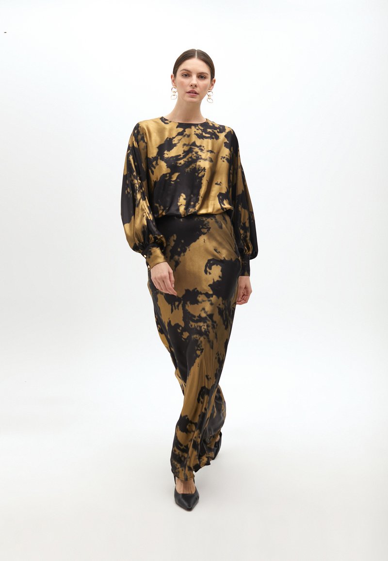 Lange goud- en zwart tie-dye jurk met een relaxed fit, lage vlindermouwen en een slanke silhouet. Gepaard met scherpe zwarte hakken.