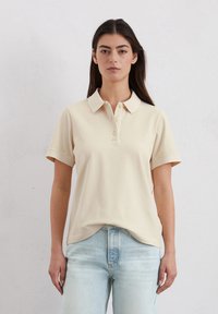 Beige polo shirt met korte mouwen, een klassieke kraag, een drie-knopen placket en een comfortabele pasvorm, gecombineerd met lichtblauwe jeans.