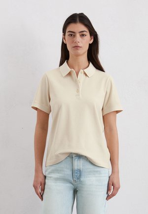 Beige Kurzarm-Polohemd mit klassischem Kragen, dreiknöpfiger Leiste und bequemer Passform, kombiniert mit hellblauen Jeans.