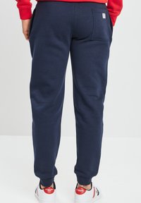 Pantalones deportivos azul marino con un corte relajado, que cuentan con bolsillos laterales y un bolsillo trasero, acabados con puños acanalados en los tobillos.