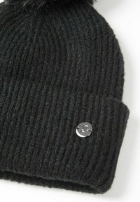 Melna ribota džemperu cepure ar salocītu maliņu un mazu apaļu metāla logo uz maliņas, uz balta fona.
