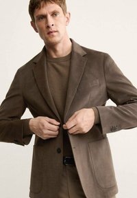 Brown blazer made of soft fabric with a notched lapel, two front pockets, and a single button closure, worn over a brown sweater.