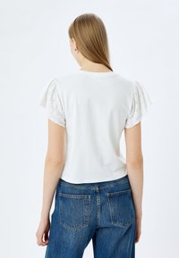 Witte top met korte mouwen en kantdetails op de pofmouwen, gecombineerd met hoogwaist blauwe denim jeans. Glad materiaal, casual pasvorm.