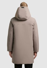 Parka color marrone chiaro, imbottita, con un grande cappuccio. Caratterizzata da una vestibilità dritta, maniche lunghe e una texture liscia e opaca.