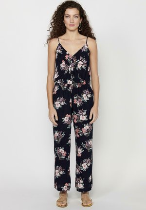Un tuta floreale realizzata in tessuto blu navy con motivi di fiori rosa e verdi, spalline sottili e una vestibilità morbida con gamba larga.