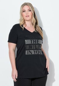 Černé bavlněné tričko s výstřihem do V a krátkými rukávy. Obsahuje stříbrný textový grafický prvek s nápisem "DIVOKOST V TOBĚ." Volný střih.