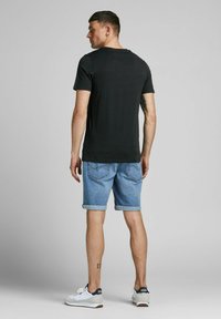 Schwarzes T-Shirt mit kurzen Ärmeln, kombiniert mit hochgekrempelten Jeansshorts. Die Shorts haben eine hellblaue Farbe und sichtbare Taschen. Weiße Sneaker mit blauen Akzenten.