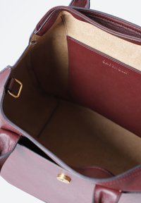 Burgundy nahkakäsi laukku, jossa on kultasävyisiä metalliosia, sisäosa sisältää vaaleanruskean mokkanahan vuoren ja lisätaskun, suorakulmainen muoto.