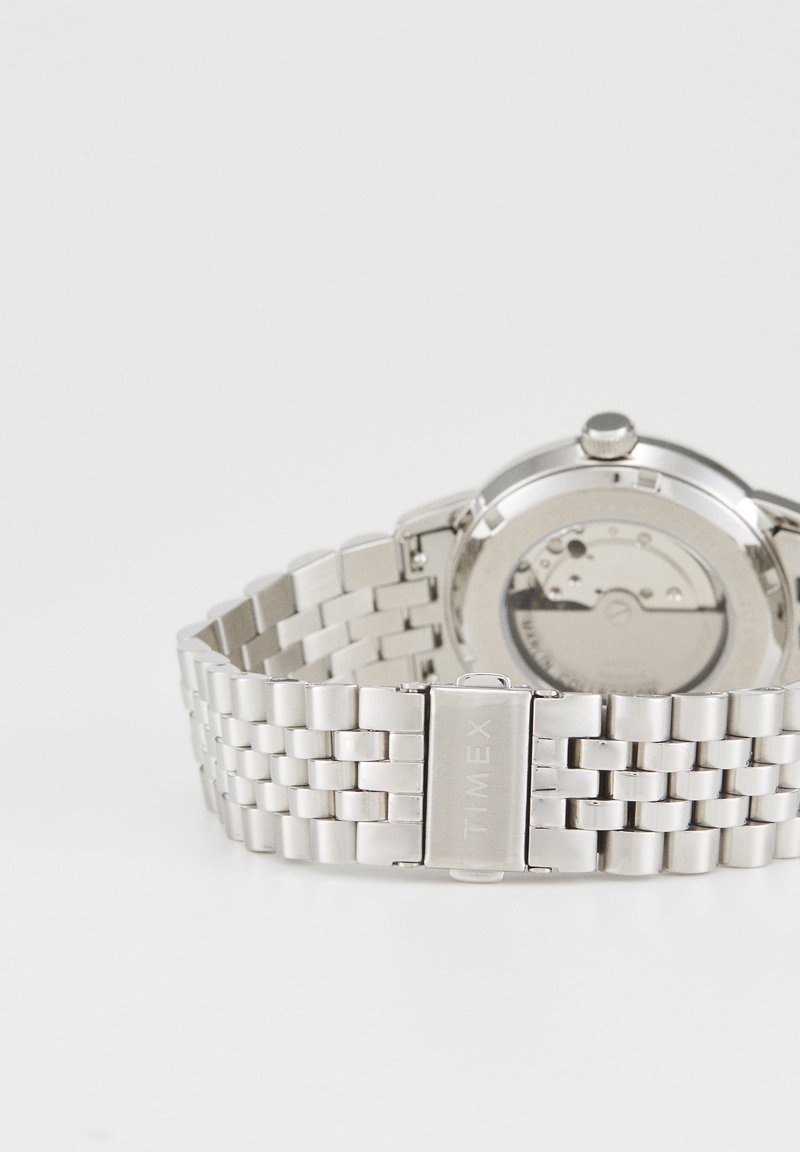 Zilverkleurig metalen Timex polshorloge met een schakelen armband en een zichtbare mechanische beweging aan de achterkant van de wijzerplaat.
