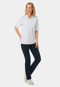 Weißes Poloshirt mit Knopfleiste und kurzen Ärmeln, kombiniert mit dunkelblauen Jeans und hellen Schuhen. Einfaches Design und Stoff.