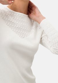 Maglietta bianca a maniche lunghe con corpo a coste, bordo in pizzo e maniche testurizzate. Il design è semplice ed elegante.