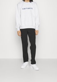 Felpa grigia in pile con logo blu sul petto, abbinata a pantaloni neri e sneakers bianche. Design semplice, vestibilità casual, texture liscia.