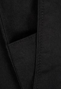 Nahaufnahme von schwarzem Denimstoff, die eine detaillierte Naht entlang einer gefalteten Naht zeigt.