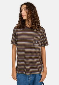 T-shirt à manches courtes rayé marron avec des bandes horizontales jaunes, bleues et blanches, poche poitrine et un patch logo noir sur la poche.
