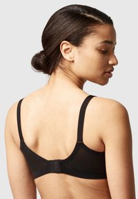 Black bra with adjustable straps, a sheer back panel, and a hook closure. Features smooth fabric and a simple design.