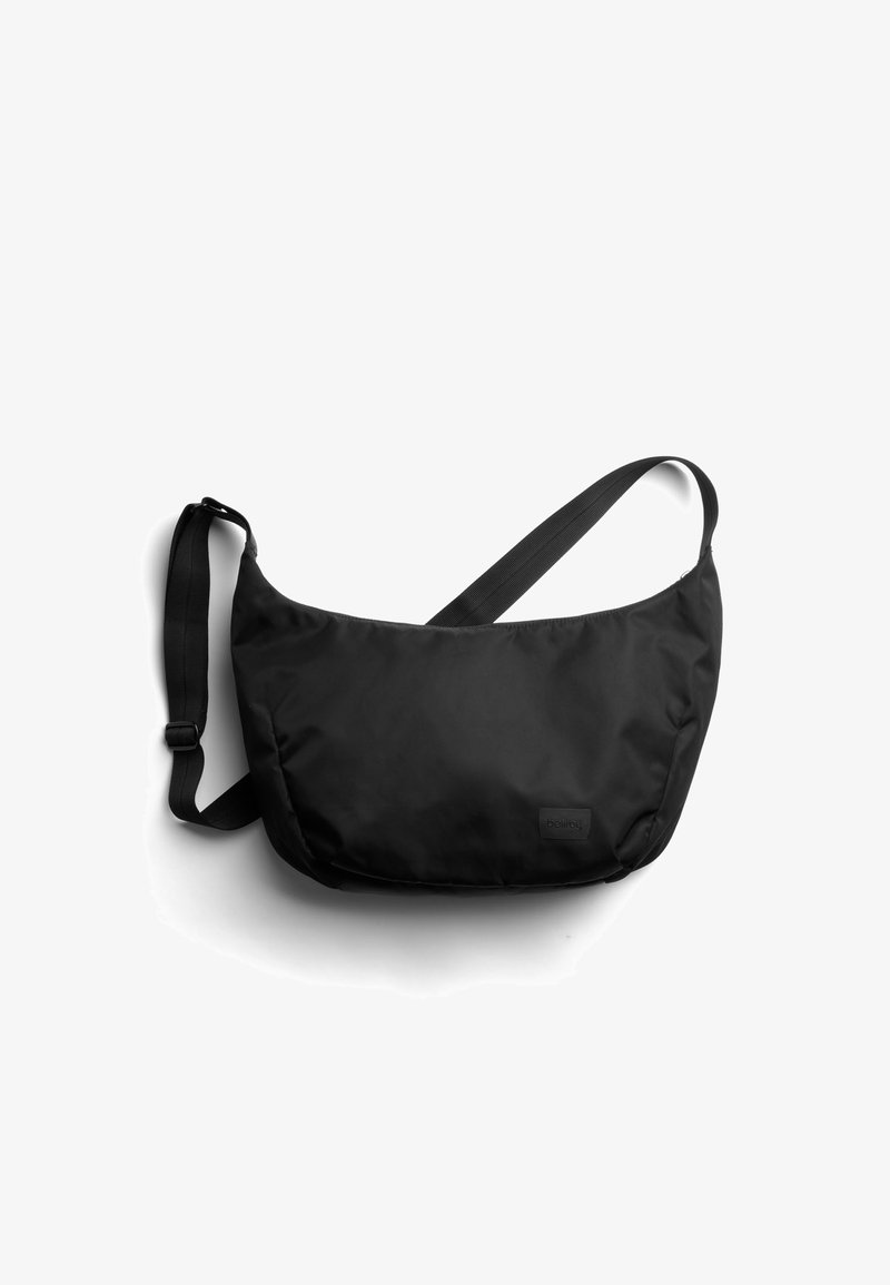 Sac à bandoulière en nylon noir avec un design doucement courbé, une sangle réglable et une petite étiquette de marque à l'avant. Texture lisse et mate.