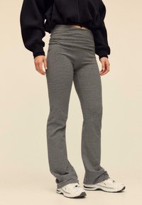 Schwarz-weiße gestreifte Leggings, figurbetont mit hohem Bund, aus elastischem Material, kombiniert mit weißen Sportschuhen.