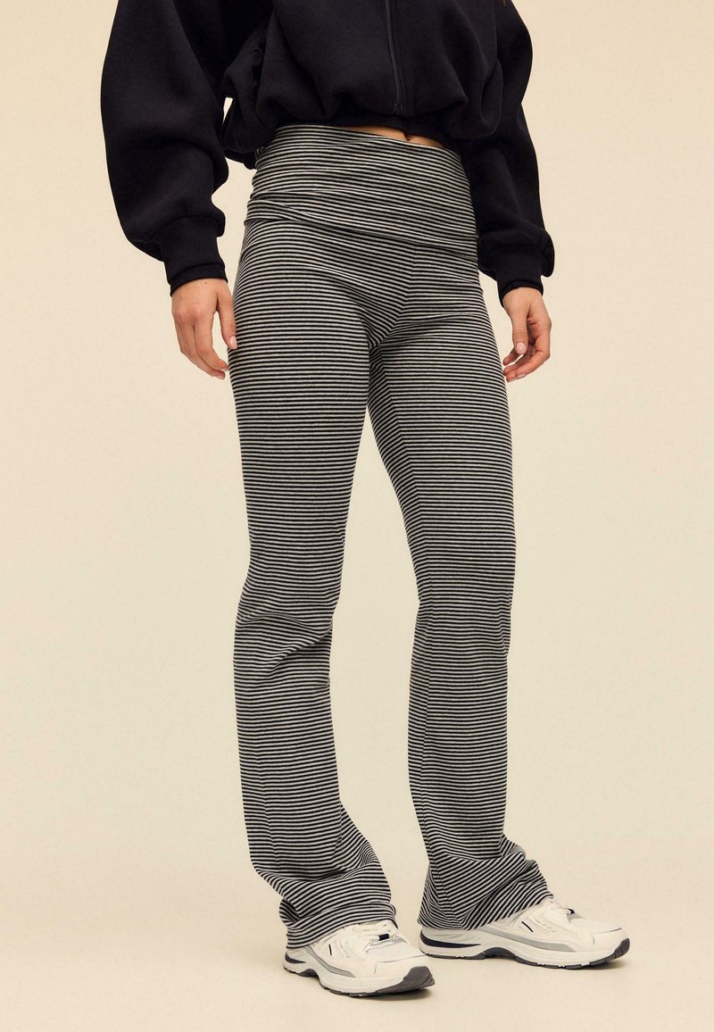 Schwarz-weiße gestreifte Leggings, figurbetont mit hohem Bund, aus elastischem Material, kombiniert mit weißen Sportschuhen.