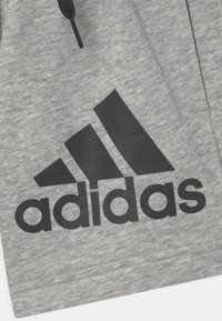Graue Sportshorts aus weichem Material, mit einem großen schwarzen Adidas-Logo und einem Design mit drei schwarzen Streifen. Mit schwarzem Kordelzug.