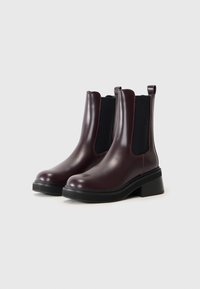 Botas de tobillo de cuero burdeos con paneles laterales elásticos, punta redonda y un tacón grueso negro. Acabado suave con tiradores para facilitar su uso.