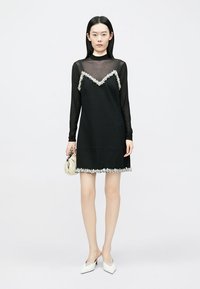 Vestido mini preto com sobreposição transparente de mangas compridas, adornado com uma barra floral ao longo do decote e da bainha. Tecido macio, design minimalista.