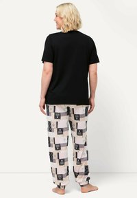 Schwarzes T-Shirt mit kurzen Ärmeln, kombiniert mit gemusterten Schlafanzughosen, die aus verschiedenen Blöcken in Pastellfarben und mit floralen Designs bestehen.