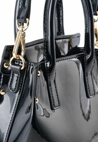 Borsa a mano in pelle verniciata nera con ferramenta dorata, forma strutturata, doppio manico e borchie decorative sui lati. Texture liscia e lucida.