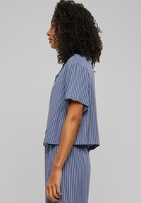 Blue striped crop top with short sleeves, featuring a loose fit and a single chest pocket, paired with a matching bottom.