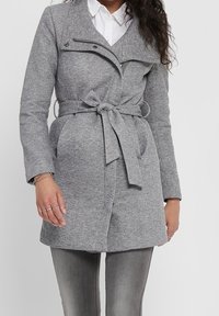 Cappotto grigio con cintura, colletto a punte, tasche anteriori e dettagli decorative con zip. Realizzato in tessuto testurizzato con una finitura liscia.
