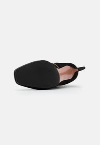 Svart mockaskor med spetsig tå, platt svart gummisula och en elegant design med en något böjd klack och subtil branding.
