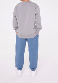 Felpa grigia con spalle scese, abbinata a joggers blu. Entrambi sono realizzati in un tessuto morbido, con polsini e vita elastici.
