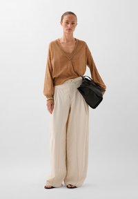 Suéter marrón de cuello en v con puños acanalados, combinado con pantalones beiges de talle alto y anchos que presentan costuras frontales. Bolsa negra con asas.