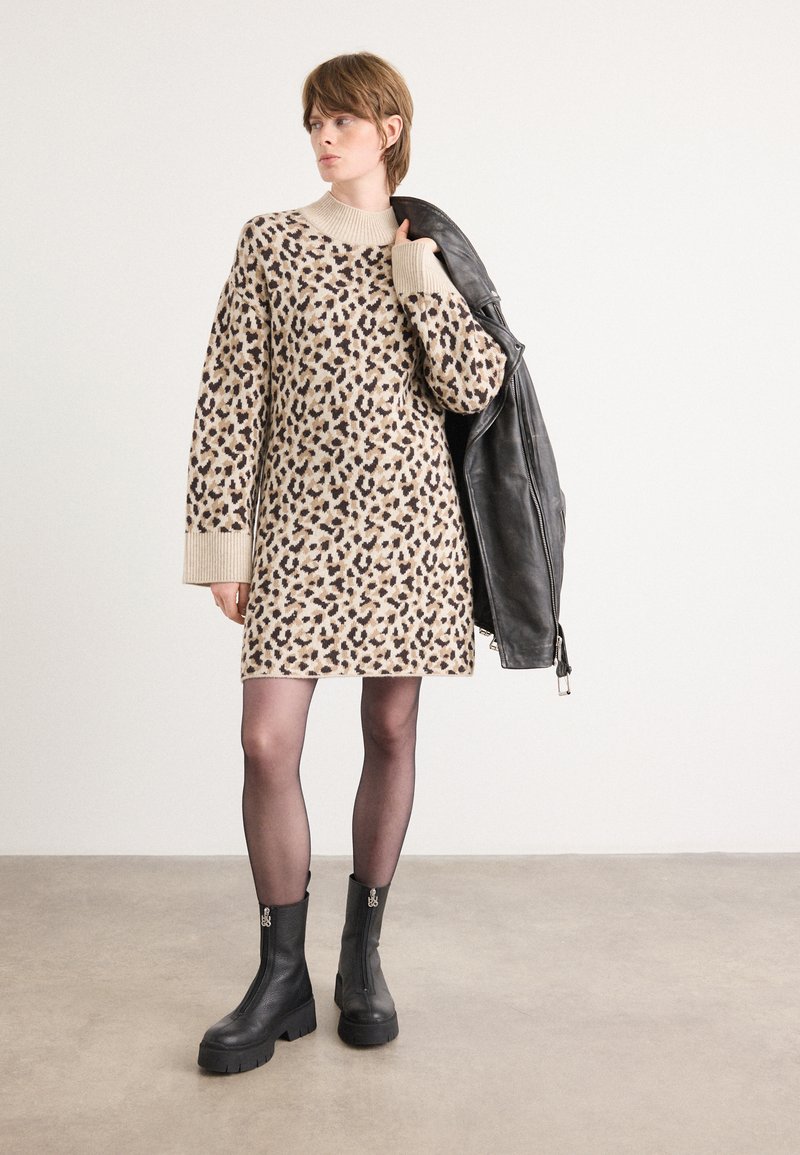 Vestido de malha com padrão de leopardo em bege, com mangas longas e decote redondo. Combinado com uma jaqueta de couro preta e botas pretas robustas.