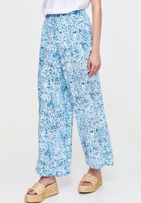 Spodnie o szerokich nogawkach w niebiesko-białym wzorze kwiatowym. Lekka tkanina, wysoki stan, zwiewny krój. W połączeniu z beżowymi sandałami na koturnie.