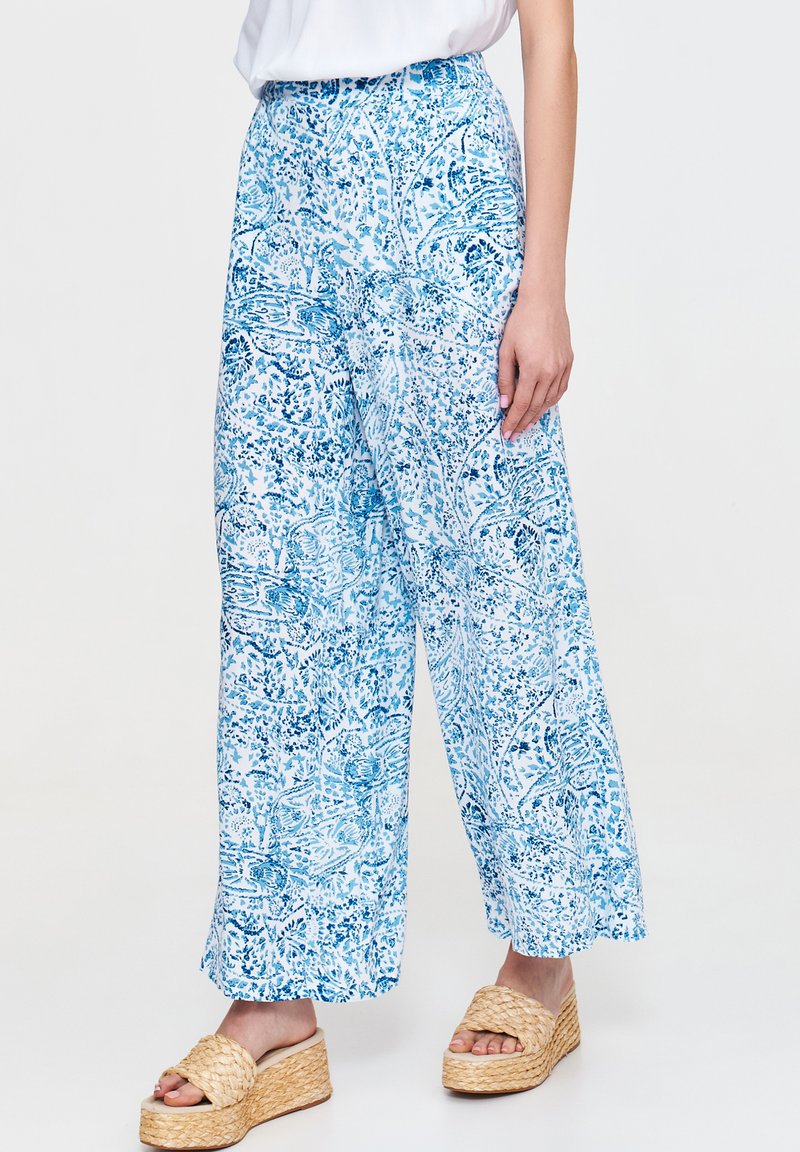 Spodnie o szerokich nogawkach w niebiesko-białym wzorze kwiatowym. Lekka tkanina, wysoki stan, zwiewny krój. W połączeniu z beżowymi sandałami na koturnie.