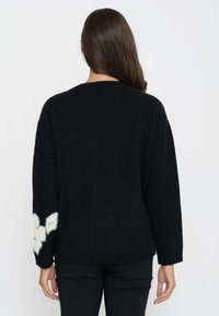Maglione nero a maglia con una vestibilità morbida, caratterizzato da un'elegante accentatura di crema sulla manica sinistra. Polsini e orlo a costine. Texture liscia.