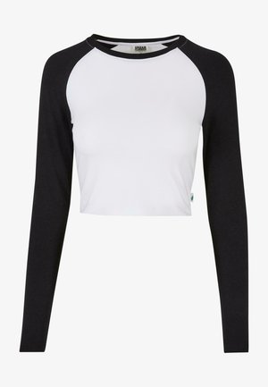 Lühike top, millel on valge keha ja mustad raglanvarrukad, valmistatud puuvillast, ümarate kaelustega ja külje sildiga detail.