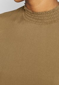 Maglione marrone a collo alto con un collo arricciato e testurizzato. Tessuto liscio con una leggera lucentezza e un design aderente.