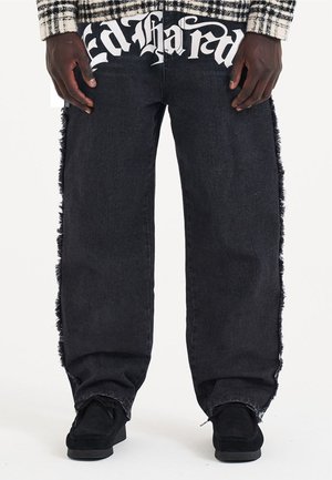 Jeans in denim nero con dettagli sfilacciati lungo i lati e grande testo bianco "Ed Hardy" sulla cintura anteriore. Design morbido e rilassato.