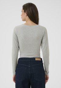 Maglietta a maniche lunghe grigia chiara con scollatura rotonda, abbinata a jeans in denim blu navy con due tasche posteriori e un'etichetta sulla vita.