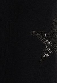 Černá látka s texturovaným pletením, na jedné straně zdobená velkou černou flitrovou hvězdou.