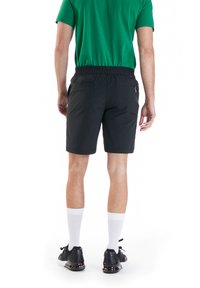 Schwarze Shorts mit elastischem Bund, seitlichen Taschen und glatter Textur. Kombiniert mit einem grünen Shirt und schwarzen Sneakers.