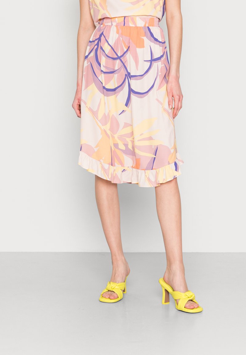 Saia midi floral com um hem rizado, apresentando cores pastel de rosa, amarelo e roxo num padrão de folhas tropicais. Combinada com sandálias amarelas.