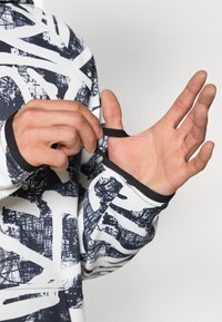 Maglietta sportiva a maniche lunghe con un motivo astratto in bianco e nero. Presenta aperture per il pollice con bande elastiche nere sui polsini per una vestibilità sicura.