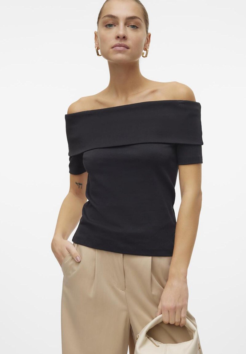 Off-shoulder svart topp laget av et glatt stoff, med korte ermer og en tettsittende silhuett. Kombinert med beige høyt liv bukser.