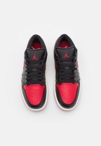 Un paio di scarpe Air Jordan nere e rosse con lacci neri e logo Jumpman rosso, viste dall'alto su uno sfondo bianco.